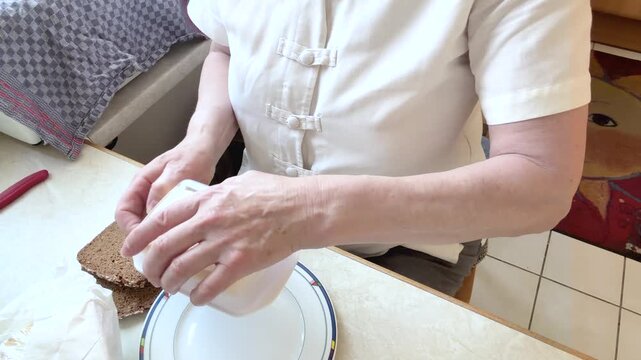 A woman opens a paper shopping bag and takes out several packaged cheese portions before placing them on the kitchen table. High-angle static shot