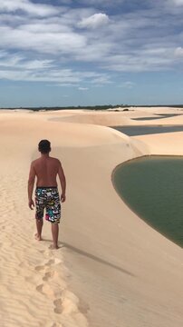 Young tourist male wearing swim trunks walking barefoot on the spectacular sand dunes of Jericoacoara National Park in Cear&aacute;, Brazil, a popular tourist destination for its lagoons and desert landscape