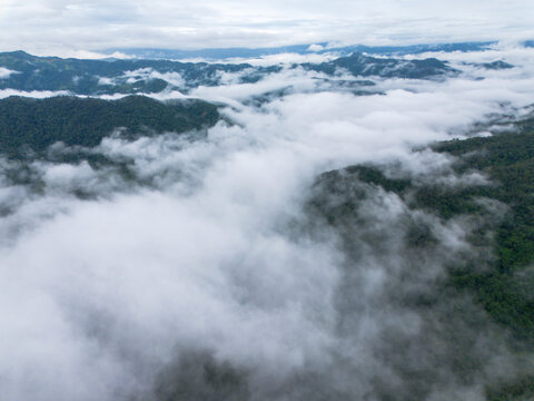 Mountain forest cloud landscape aerial view with mist drifting across rugged green ridges beneath overcast sky, creating tranquil natural wilderness panorama for travel and environment themes