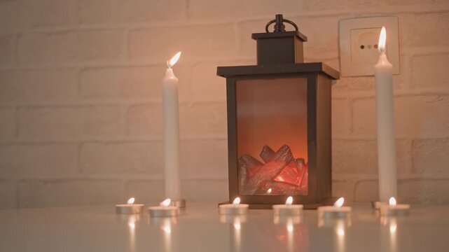 Metal lantern with glowing embers sits centered on glossy countertop between two burning taper candles while tealights flicker nearby, creating warm reflections, gentle movement, and cozy interior