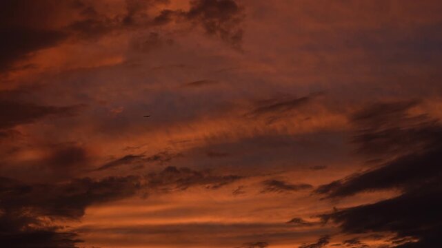 Cinematic stock video footage of dramatic sunset clouds moving slowly across a warm orange sky, creating a peaceful and serene atmosphere for background use. An airplane flys across the frame.
