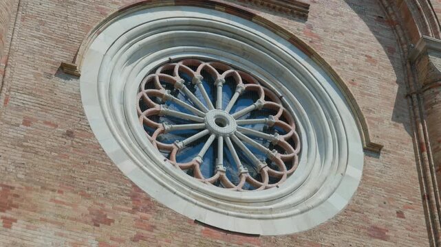 Rose window gothic cathedral facade close up detail on an ancient brick church. Ornate stone architecture showing historical religious heritage on a sunny summer day, handheld pan shot.