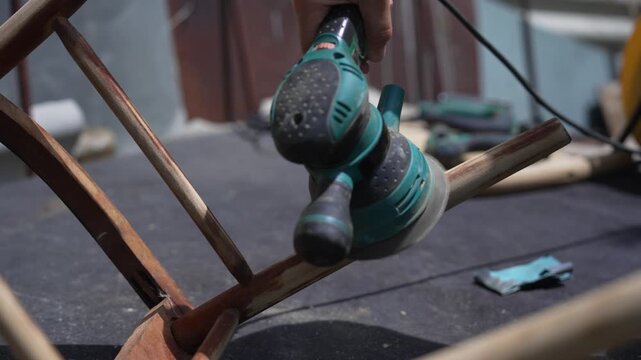 Female Craftsperson Using an Electric Sander to Restore an Old Wooden Chair