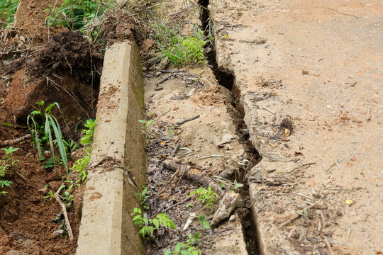 Erosion damage concrete road soil collapse drainage channel exposed earth cracked pavement shows dangerous infrastructure failure after heavy rainfall and creates serious access risk rural