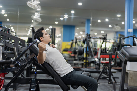 Young Asian man in white t-shirt performing upper body exercise on incline chest press lever machine in modern gym.