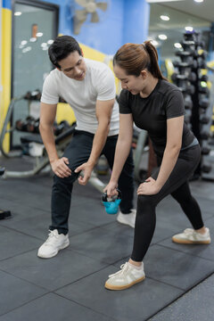 Asian woman working out on chest press machine with male personal trainer assistance in gym