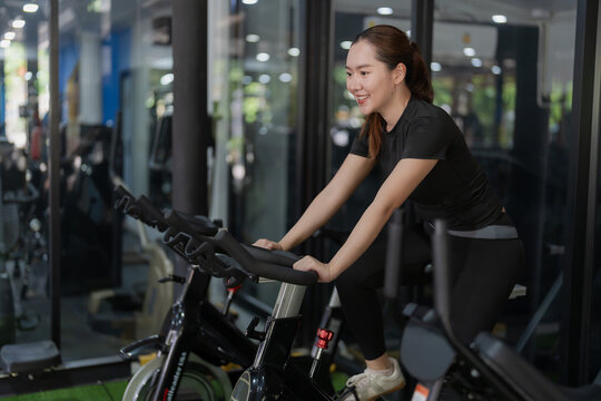 Smiling Asian woman riding stationary exercise bike in gym