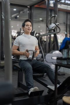 Asian man performing seated cable row exercise on machine in gym