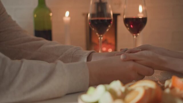 Close tabletop view of two people holding hands across candlelit dinner table, palms gently clasped and fingers slightly interlaced conveying tenderness and reassuring connection