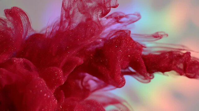 Vibrant red ink swirling in water with sparkling particles and colorful blurred background
