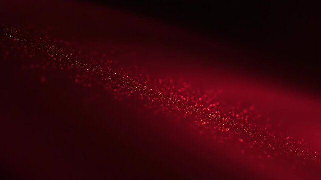 Close up of red glitter particles sparkling on dark surface with soft glowing light and bokeh effect