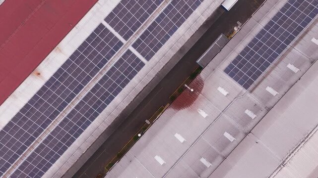 Aerial drone view of a large industrial complex in Indonesia with extensive solar panels installed across factory rooftops. The geometric arrangement of buildings, photovoltaic panels, roads, and surr