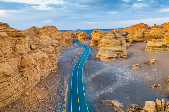 Winding highway cuts through yardang landforms in Dahaidao, Hami, Xinjiang, China, under a blue sky.