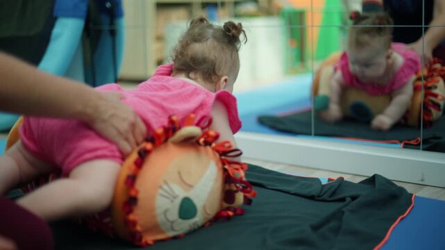 Baby girl in pink dress engages in developmental therapy, improving motor skills and sensory perception by observing her reflection