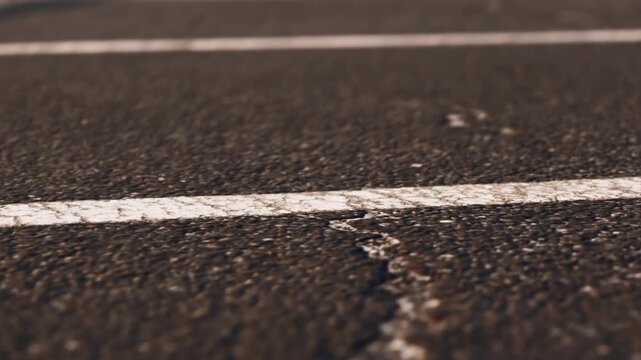 A close view shows thin white lines on an asphalt road. The scene captures the texture and detail of the surface. The setting suggests a street or parking area.