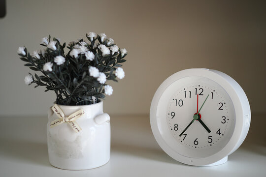 Simple clock and flower pot are on a white shelf