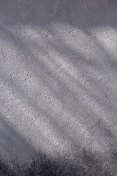 close-up view of a weathered gray concrete surface with subtle variations in tone and rough texture. Soft natural lighting highlights the uneven plaster, fine imperfections, stains, and aged areas acr