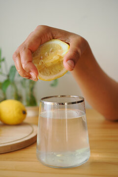 Squeezing lemon into a glass of water on a wooden table