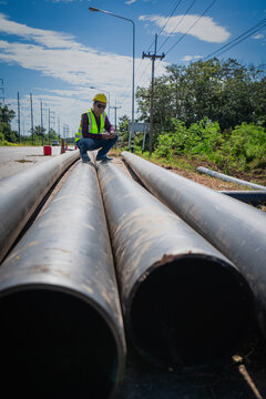 Asian construction workers inspect PE pipes before installing drainage systems. HDPE pipes are used for water and gas supply systems at construction sites.