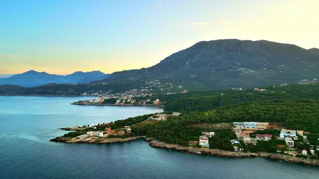 Aerial view of the adriatic coast at sunset, showing coastal towns, green hills, and mountains.