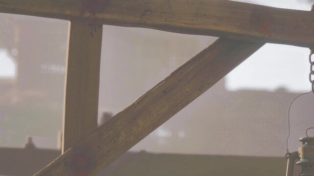 In a rustic area, a wooden frame supports a lantern. Sunlight shines through, creating a warm atmosphere. The scene shows details of the construction and placement of items.