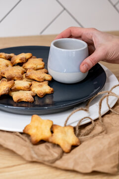 Tasty breakfast. Yummy food. Woman hand holding drink cup above cookies plate served on wrapped craft paper jute rope at rustic kitchen.