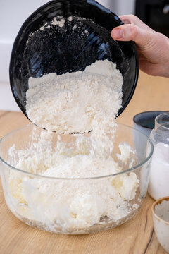 Preparing dough. Adding flour. Woman chef hand pouring culinary ingredient in glass bowl cooking tasty homemade pastry meal at kitchen table.