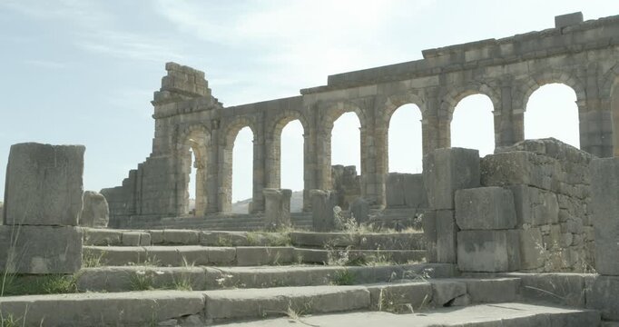 Static ground-level view of stone steps leading to the arcaded Basilica of Volubilis, highlighting Roman civic architecture at Morocco's UNESCO World Heritage archaeological site.