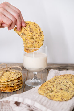 Homemade snack. Rustic treat. Female eater hand dipping crunchy round cookies in milk glass on table with biscuits served on napkin.