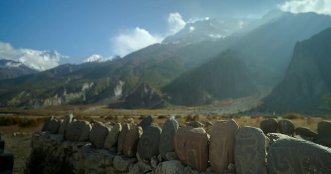 Annapurna Circuit, Manang, Nepal, Carved Buddhist mani stones with a soft blurred Himalayan mountain range in the background.
