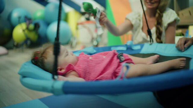 Baby girl resting in a sling for rehabilitation, improving motor development and sensory integration with physical therapy