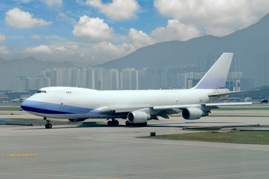 Large cargo heavy airplane taxis on the runway ready surrounded by majestic mountains and modern city buildings