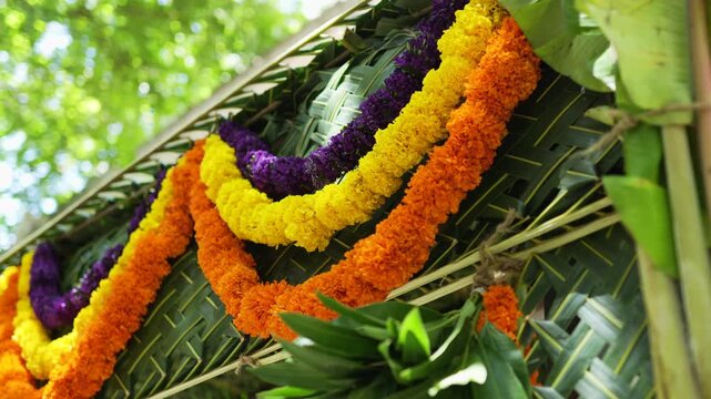 Bright marigold and flower garlands hang across a woven coconut leaf chapra roof outside a South Indian home in slow motion.
