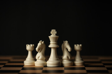 white chess pieces (king, knights, rooks) aligned on a wooden board, black background © geargodz