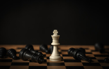 white chess king surrounded by fallen black pieces on wooden board © geargodz