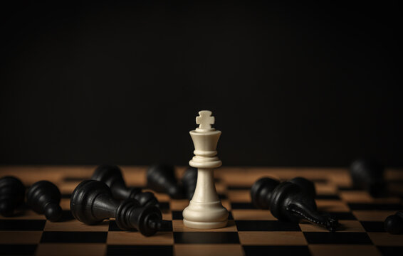 white chess king surrounded by fallen black pieces on wooden board