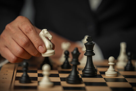 business hand arranging chess knight on wooden board, game strategy