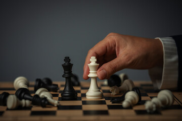 business hand placing white chess king facing off black on a board surrounded by pieces © geargodz