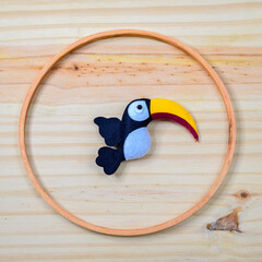 Handmade felt toucan bird decoration arranged inside a circular wooden ring on a light wooden background © nilanka