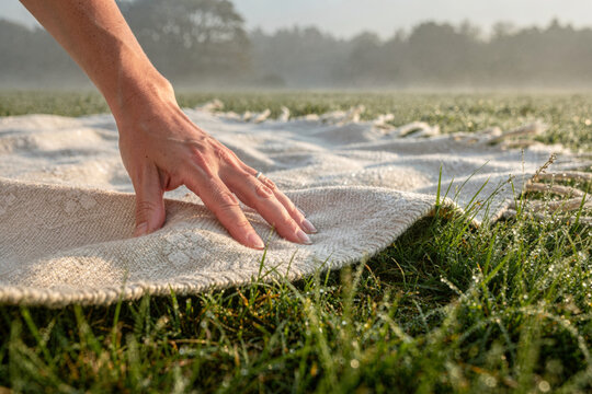 Hand Touching Woven Blanket on Dewy Morning Grass Field
