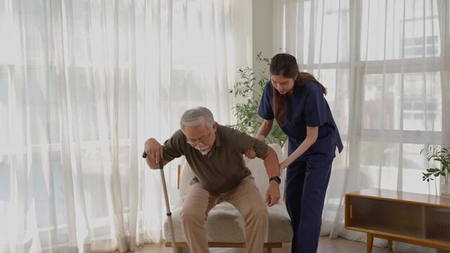 Older man using walking cane with healthcare worker and caregiver providing support, mobility rehabilitation, daily care, and compassionate assistance in bright home interior near window and sofa