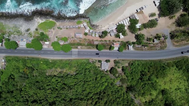Aerial top down view of a coastal highway running along a tropical beach and lush green forest