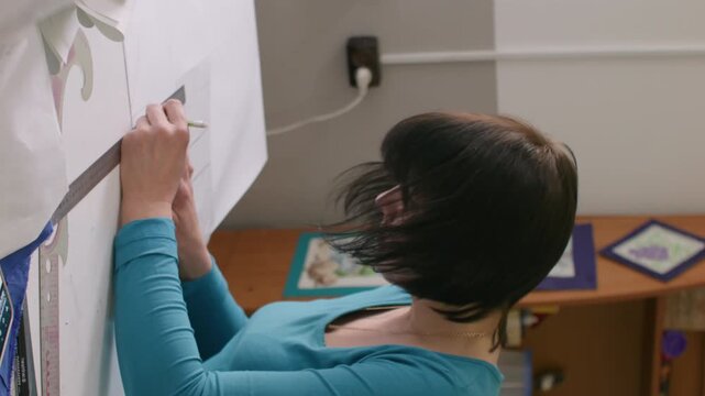 Vertical video. Dressmaking process. Tailor desk. Woman hand creating garment patterns with ruler making notes on paper in clothes studio interior.