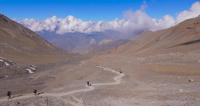 Annapurna Circuit, Manang, Nepal, drone tracking shot of trekkers hiking along a winding trail across high altitude rocky terrain in the Himalayas.