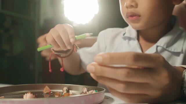 Mother gently guides her child while sharpening a colored pencil, teaching hand coordination, fine motor skills, concentration, independence, and responsibility.