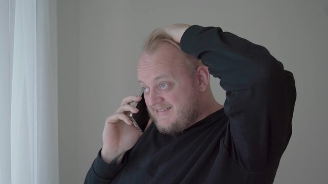Concerned man on a smartphone call holds his head and looks uneasy, reacting to unsettling or suspicious news.