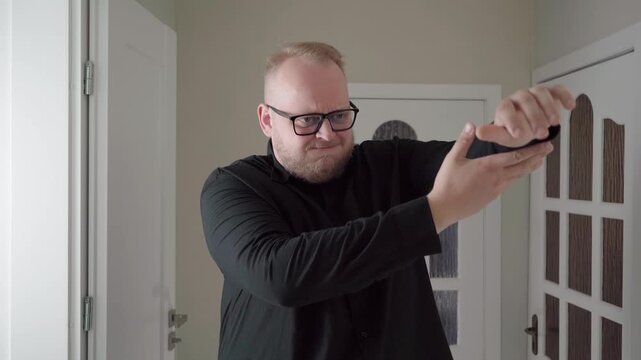 Adult man with glasses strains to raise a rigid arm using his other hand, acting out shoulder mobility problems.