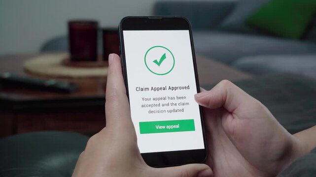 Hands hold a smartphone showing a Claim Appeal Approved message with a green check mark and View appeal button on screen.