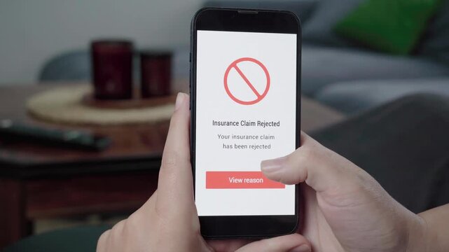 Hands hold a phone as an Insurance Claim Rejected message appears with a red prohibition icon and View reason button.