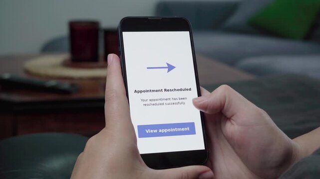 Close-up of a person using a home app as an Appointment Rescheduled confirmation alert appears with a blue View appointment button.